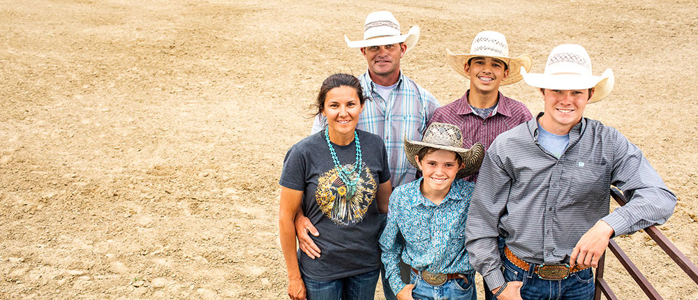 Family poses on the rodeo grounds, wearing cowboy hats and jeans