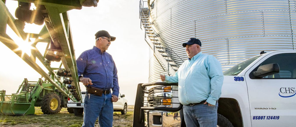 Farmer and agronomist talking near farm equipment and grain bin 