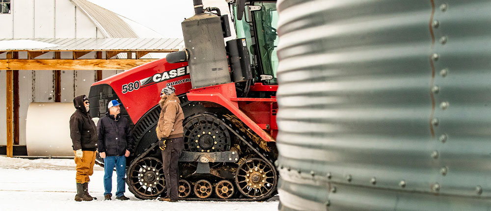 Art and Joe Ridl stand next to large red tractor while talking with a Cenex certified energy specialist