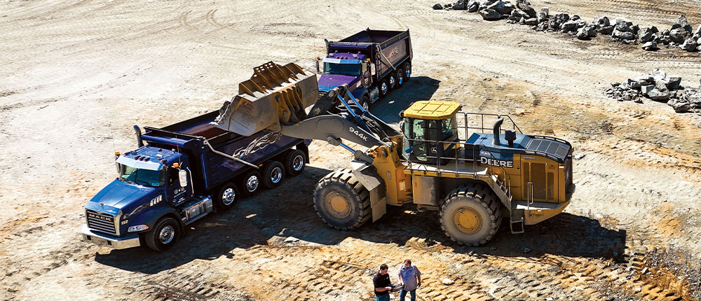 An end loader dumps rock into a dump truck in a rock quarry.